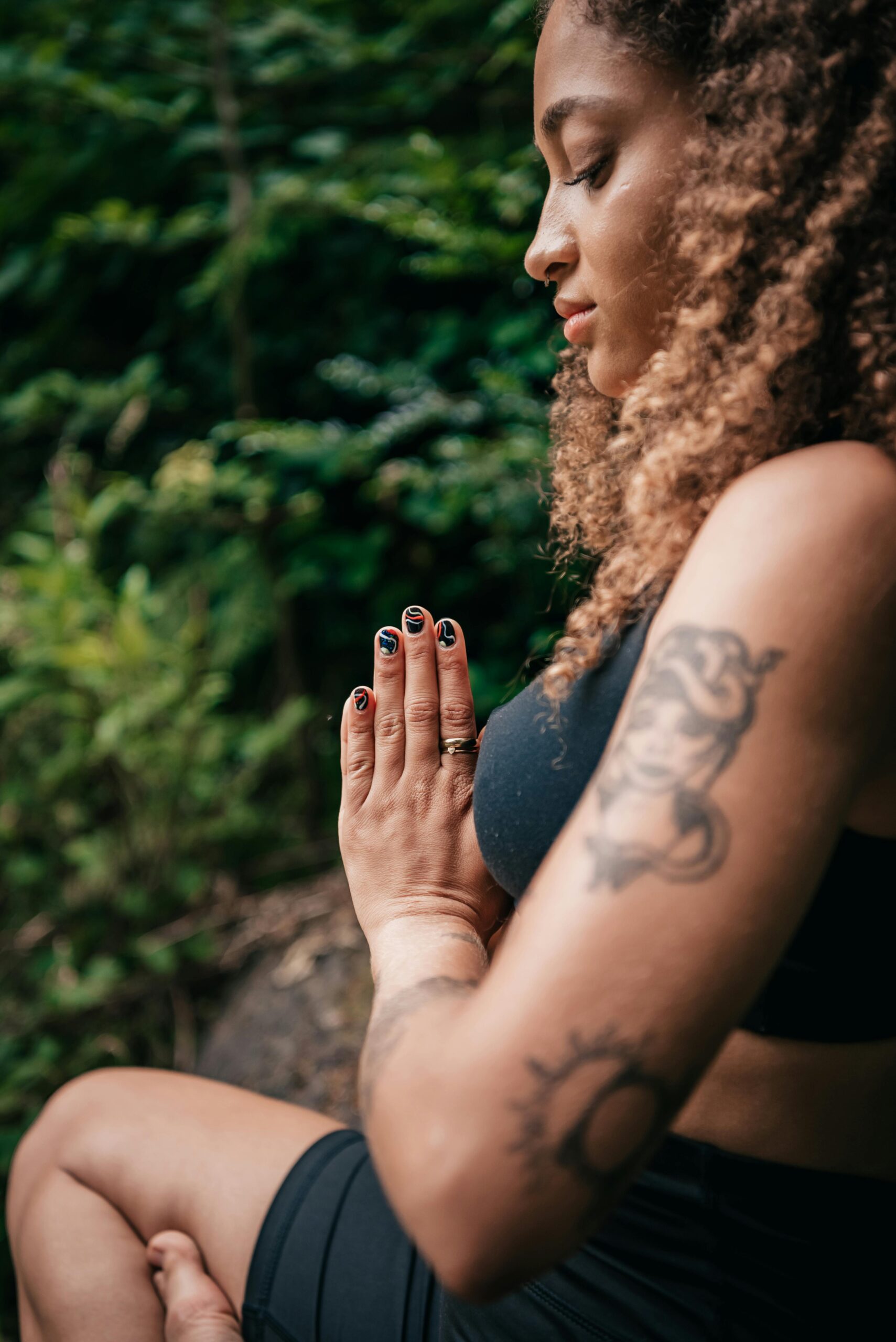 Lähikuva sivulta meditoivasta naisesta. Hän istuu jalat ristissä, Kädet yhdessä. Katse on käsiä kohti.